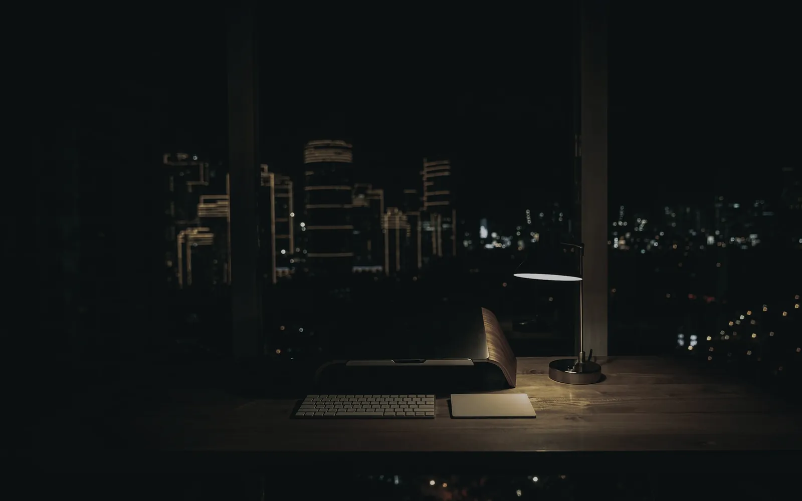Desk lamp on an empty desk at night, city towers lit beyond the window